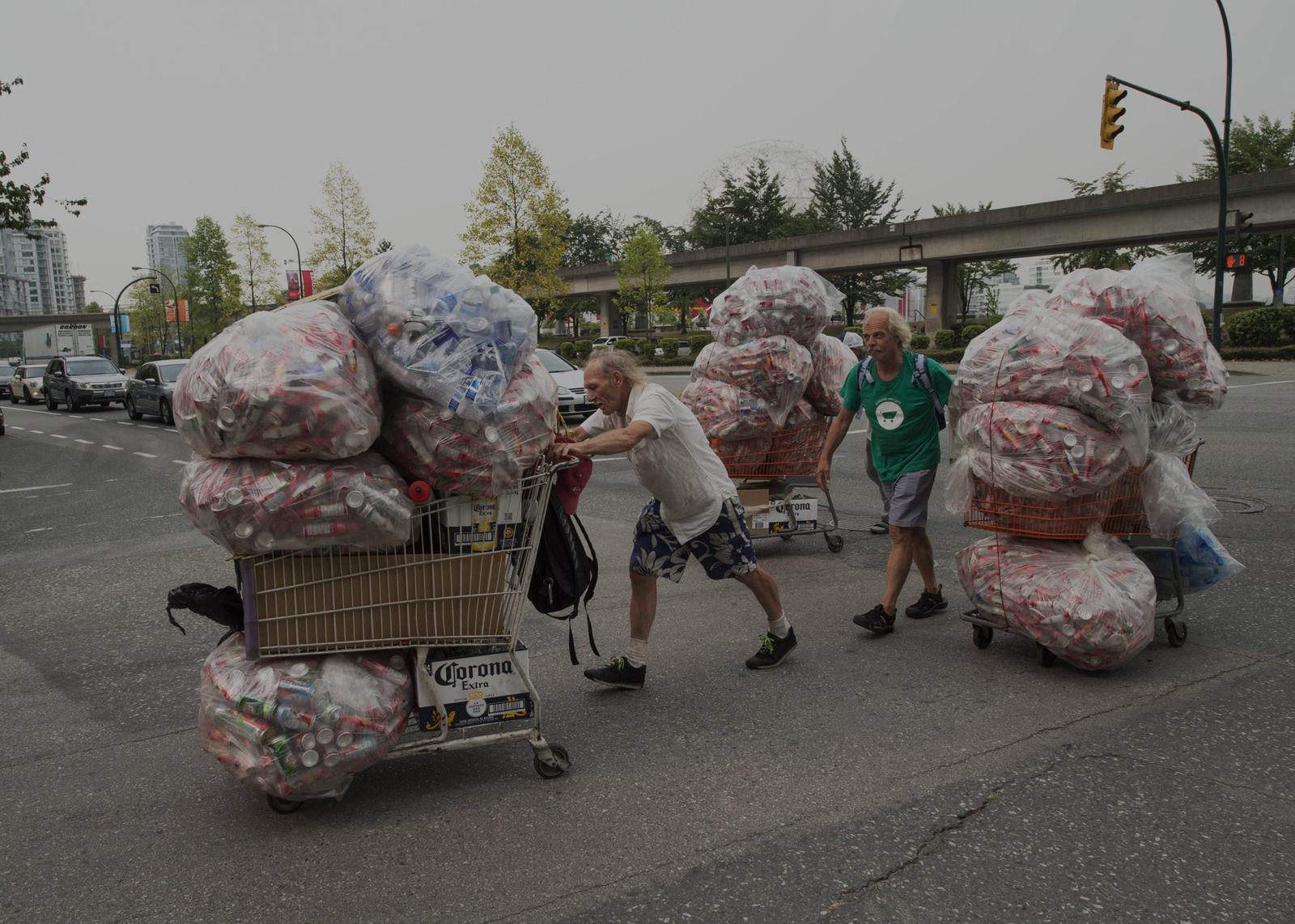 Binners pushing carts loaded with bags of recyclables through Vancouver, with a Binners' Project team member alongside